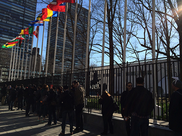 Camp attendees line up outside the UN, under the flags of many nations.